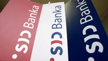 Tri viseče zastavice v rdeči, beli in modri barvi prikazujejo logotip in napis ‘SID banka’. Zastavice so postavljene pod različnimi koti in visijo s stropa.